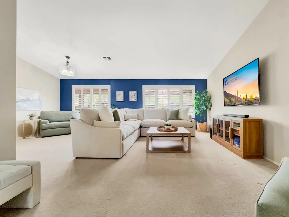 A comfortable living room centered around a large sectional sofa, a sleek coffee table with decorative accents, a wall-mounted TV, and a potted plant. The space feels welcoming and perfect for movie nights or informal gatherings.
