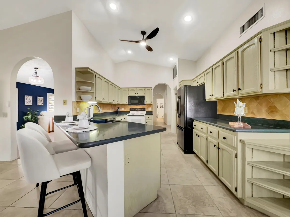 This image features a modern kitchen with a prominent kitchen island, bar stools, sleek black appliances, and stylish light fixtures. The open layout invites both cooking and gathering, capturing the heart of a chef's kitchen where family and friends can easily interact.