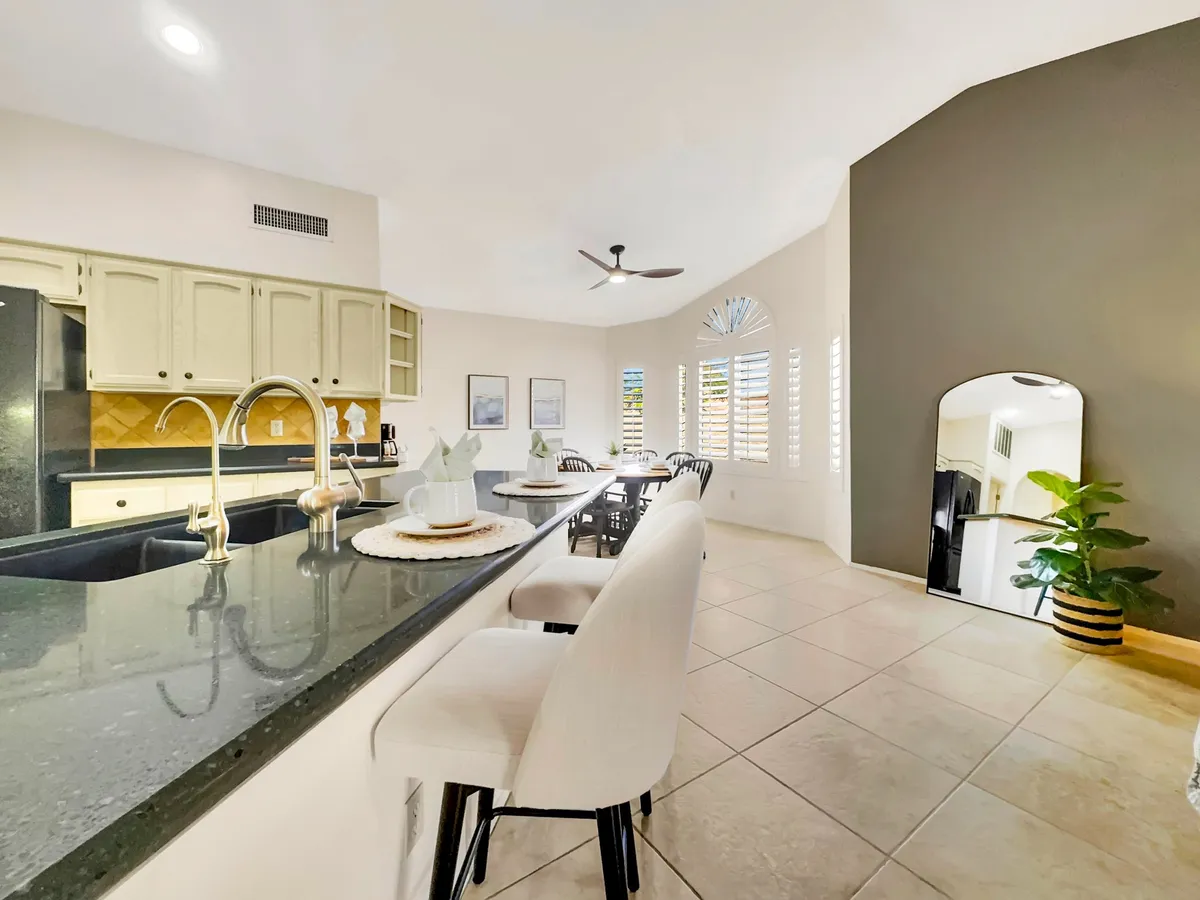 A seamless view of the kitchen island with bar stools leading into the adjacent dining area. Window shutters and an indoor plant offer a relaxed, homey atmosphere, while the setup encourages casual meals and socializing.