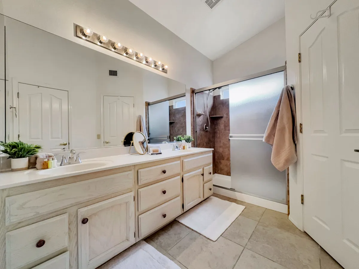 A modern, serene bathroom with a double sink vanity, a large mirror, a spacious shower area, and a decorative plant. The room feels inviting and functional, perfect for self-care routines and fresh starts to the day.
