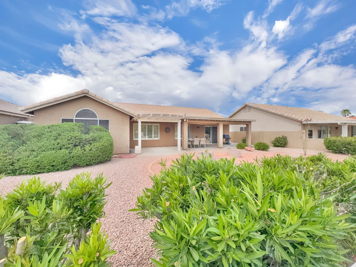 A welcoming front porch bordered by a landscaped garden and under an expansive blue sky, inviting residents and guests to relax or socialize outdoors. The scene highlights both the tranquil and community-oriented aspects of resort living.