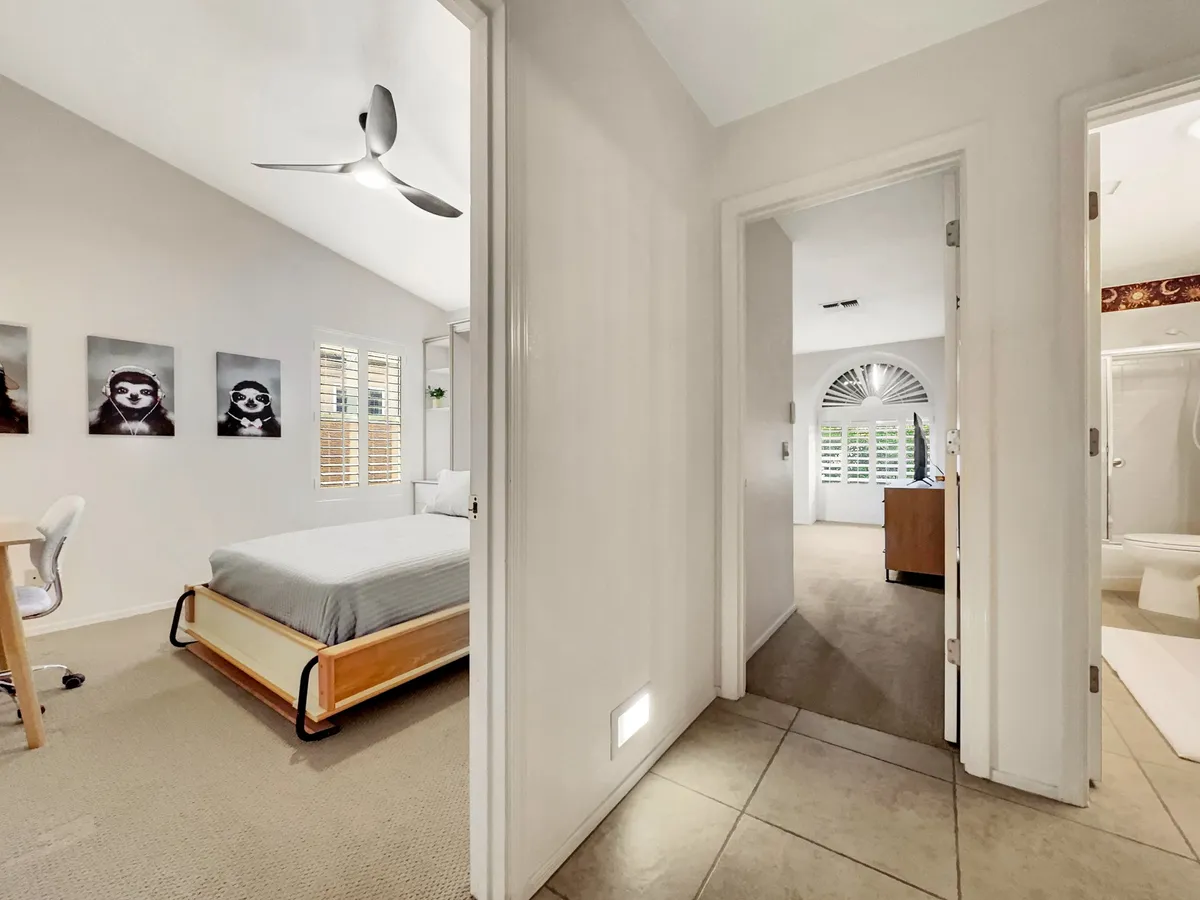 A serene bedroom that integrates a comfortable bed and a working desk, with soft wall art and inviting decor. The room is bright and airy, suggesting a versatile space for both rest and remote work.