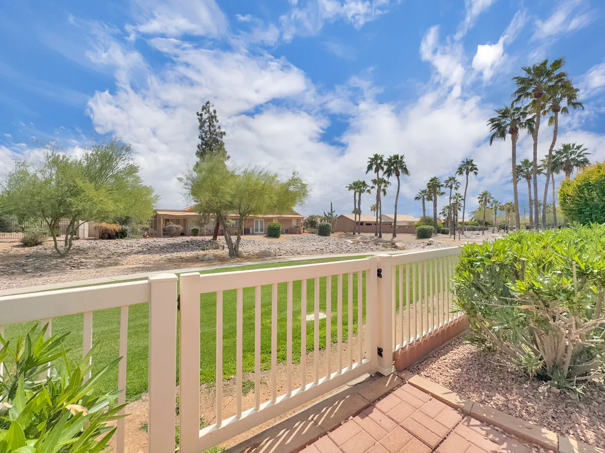 A tranquil exterior scene with green grass, palm trees, and a white fence stretching across a captivating landscape. The space is perfect for relaxing outdoors, hosting gatherings, or taking in the sunset—paralleling the open, inviting ambiance described in the section.