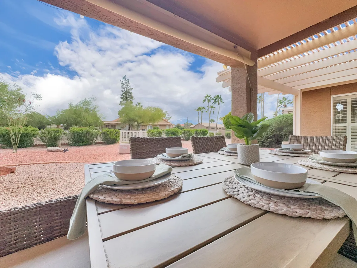 An inviting outdoor dining area set with place settings under the open sky, surrounded by lush greenery. The atmosphere is tranquil yet social, hinting at the possibility of group gatherings, relaxed meals, or simply enjoying the outdoors in a serene resort-like setting.