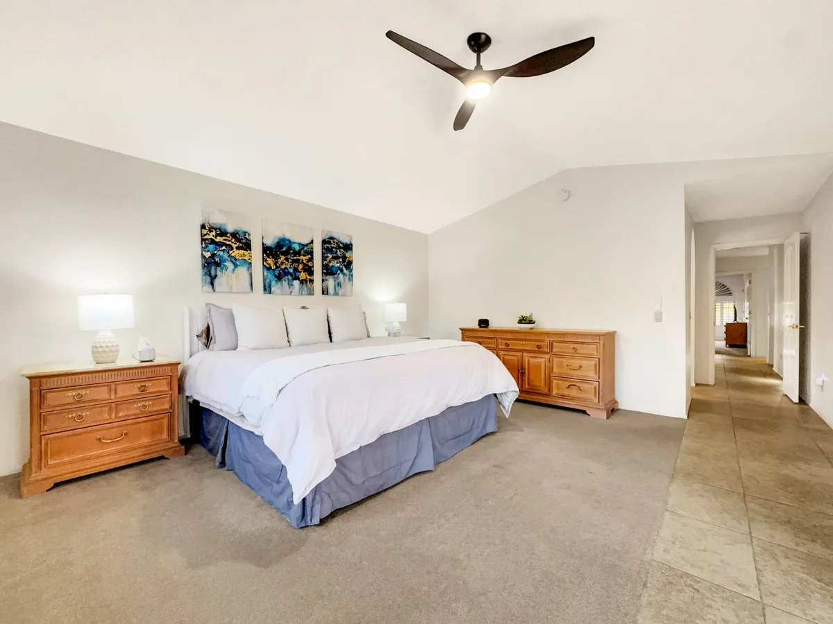 This image features a serene primary bedroom with a king-sized bed, artwork above the headboard, and wooden dressers. The space is bright and neatly arranged, evoking a sense of calm and comfort tailored for restful nights and relaxing mornings.