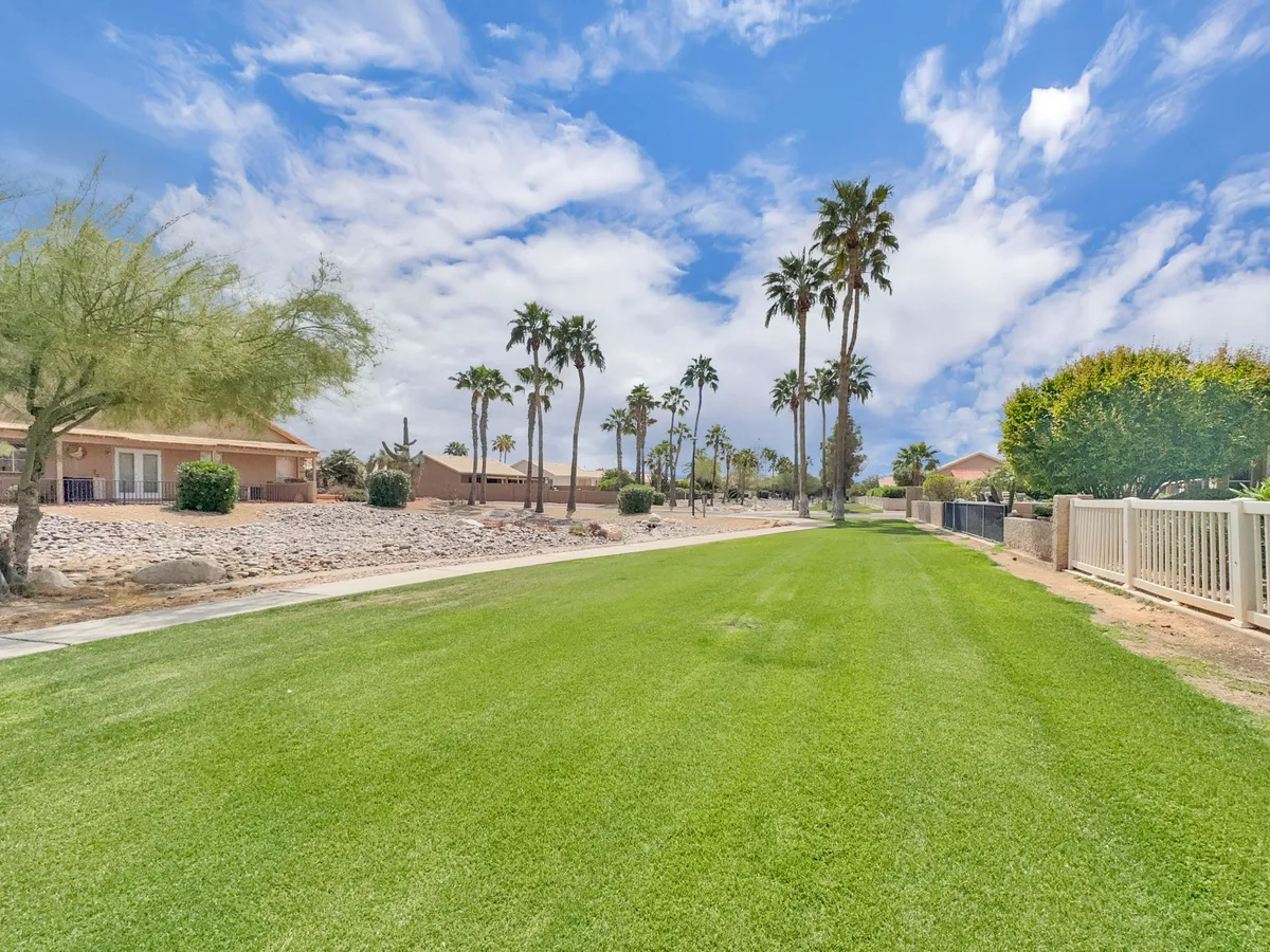 This exterior image features a lush green lawn bordered by tall palm trees and a gently winding pathway. The atmosphere is relaxed, with ample open space ideal for walking or unwinding after a round of golf. Sunset views framed by palm trees evoke the scenic desert landscape described in the section.